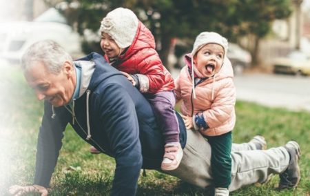 Elderly man joyfully exercising with young children on his back, demonstrating active aging and senior fitness.